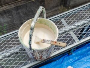 足場の上でハケが入った使い込まれた白い塗料バケツ