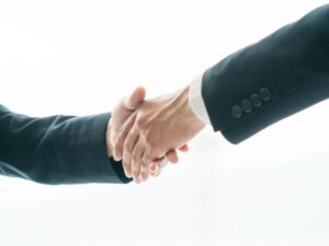 スーツ姿の二人が白い背景の前でしっかりと握手を交わしている