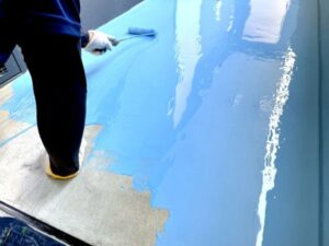 屋上床面にローラーで青色防水塗料を塗布する作業
